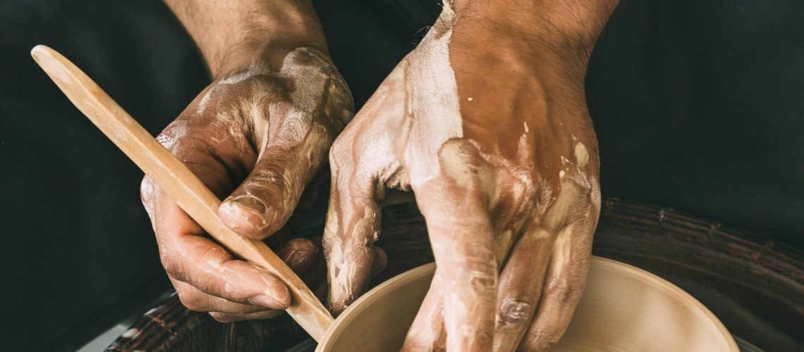 Man is sculpting a bowl behind a rotating potter's wheel